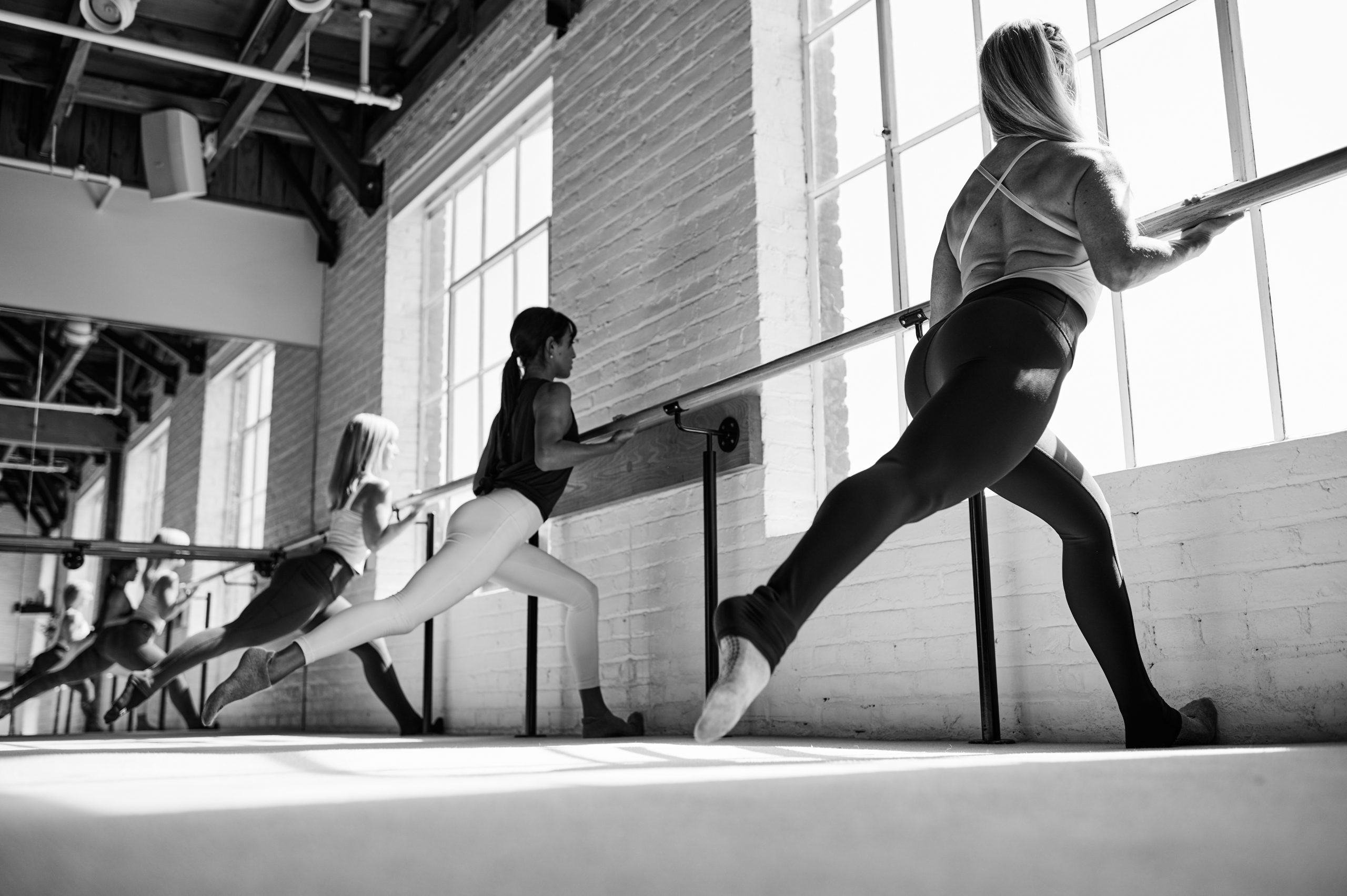 Black and white image of Bar Method members doing split squats at the barre