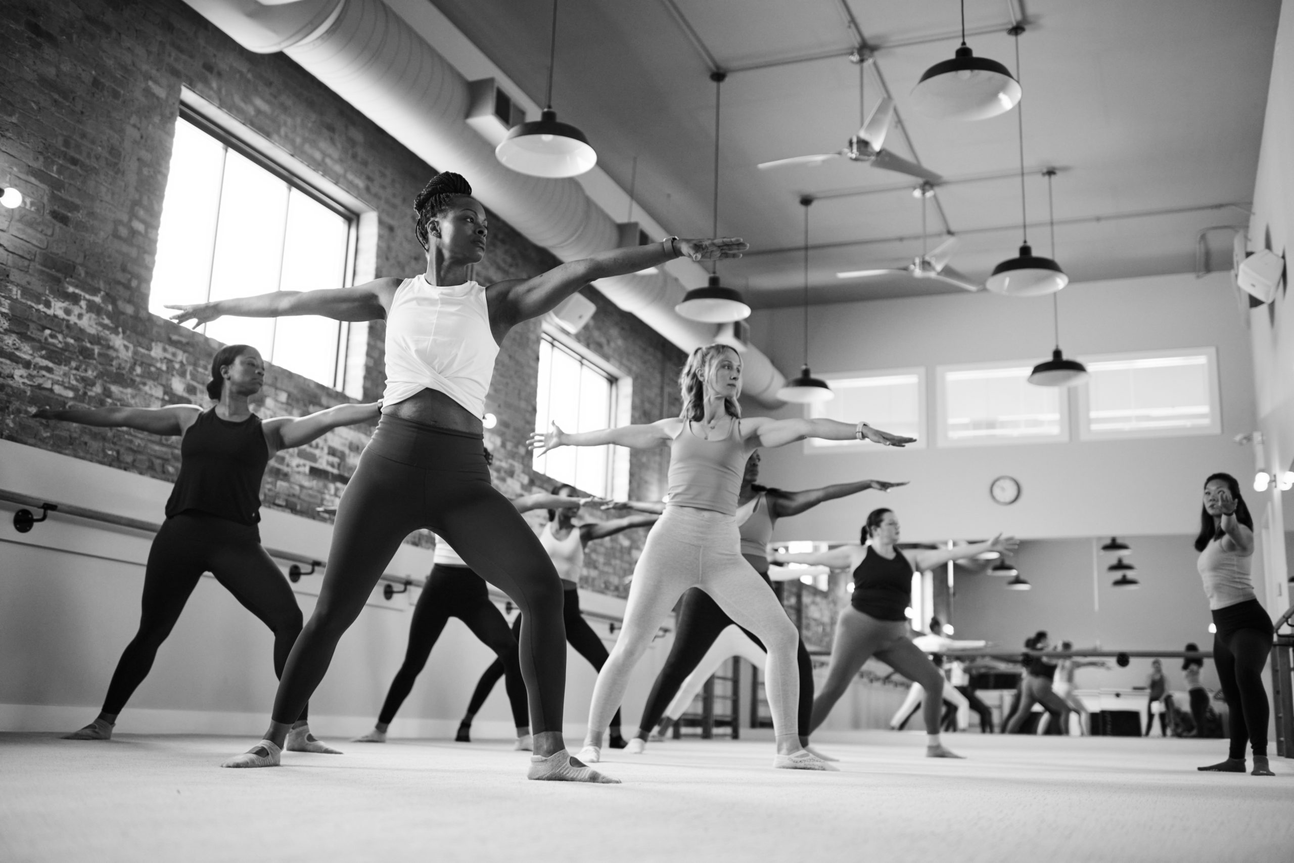 Group of women working out in Bar Method Studio practicing warrior pose.