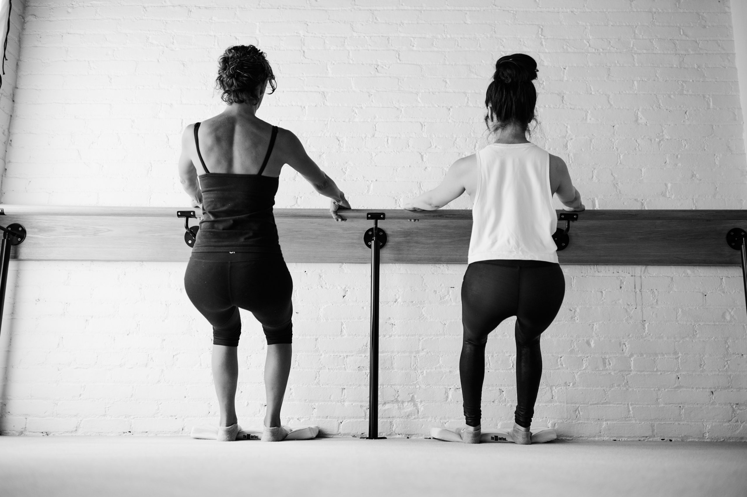 Black and white image of two people squatting at the Barre in Bar Method studio.