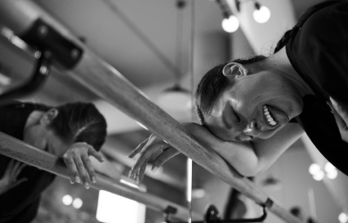 Black and white image of woman smiling and resting her head on the Barre after completing a workout